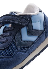 Blå sneaker med nät- och mockamaterial, med zickzackmönstrade detaljer, platta snören och en vadderad krage för komfort.