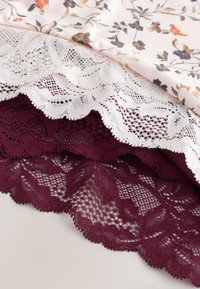 Lillemustriga kangas, millel on valged ja burgundi pitsäärised. Pitsidel on lainelised servad ja keerukad mustrid. Tekstuuriga, kergekaaluline materjal.