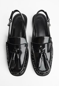 Schwarze Slingback-Schuhe mit glänzendem Finish, die eine Loafer-Style-Oberseite, Quastenakzente und geflochtene Details entlang der Kanten aufweisen.
