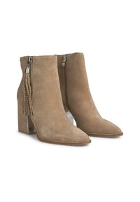 Botines de ante beige hasta el tobillo con punta afilada, tacón bloque, cremallera lateral y borlas decorativas con acentos plateados.