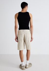 Sort tanktop, beige kordfløjs shorts med lige snit, to baglommer. Modellen har lette sneakers og hvide sokker på.