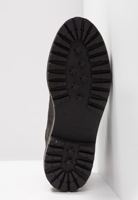 Suela de goma negra de un zapato con un patrón de estrellas, surcos profundos y logo de marca. Talla 37 grabada en el borde.
