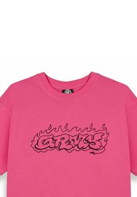 Camiseta de algodón rosa con un diseño gráfico en forma de llama negra y texto estilizado en el centro. Cuello redondo y mangas cortas.