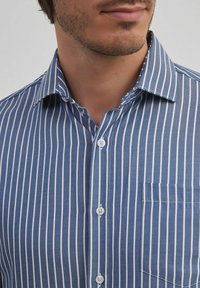 Chemise à rayures bleues et blanches avec un col classique, en tissu coton, et une poche poitrine unique. Comprend des boutons blancs et une texture lisse.