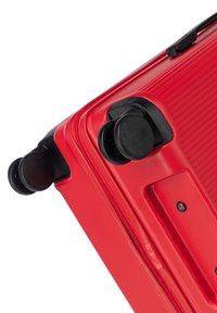 Valigia rigida rossa con superficie texture, maniglie laterali e doppie ruote nere per la mobilità. Design compatto con chiusura a zip.