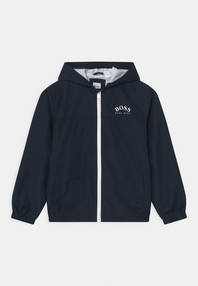 Chaqueta cortavientos azul marino con capucha, con cierre frontal de cremallera, logo blanco en el pecho y puños y dobladillo elásticos.