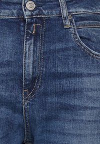 Jeans dżinsowe w ciemnoniebieskim kolorze o klasycznym kroju. Cechy to zapięcie na guzik, kieszenie z przodu i kontrastowe przeszycia.