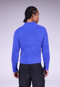 Pull en laine bleu flou avec une texture côtelée, un col montant et une silhouette ajustée. Associé à un pantalon cargo noir usé.
