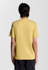 Gul bomulds t-shirt med rund hals og korte ærmer, vist fra ryggen med en glat tekstur og minimalistisk design.
