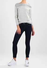 Top a maniche lunghe grigio e bianco a righe, jeans skinny blu scuro e sneaker bianche con dettagli grafici.