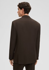 Bruine, op maat gemaakte colbert met een gladde textuur, revers met inkeping en een enkele achterkantsplit. Voorzien van mouwen met knopen en een getailleerd silhouet.