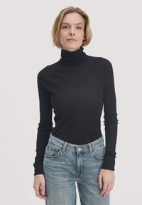 Schwarzer, gerippter Rollkragenpullover mit langen Ärmeln, der eine enganliegende Passform und einen hohen Kragen aufweist. Kombiniert mit hellblauen, hoch taillierten Jeans.