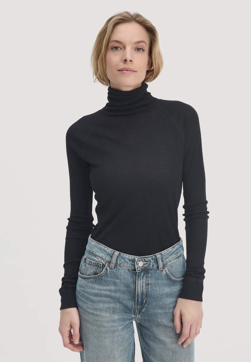 Schwarzer, gerippter Rollkragenpullover mit langen Ärmeln, der eine enganliegende Passform und einen hohen Kragen aufweist. Kombiniert mit hellblauen, hoch taillierten Jeans.