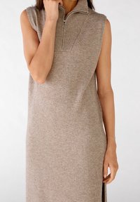Robe sans manches en tricot beige avec un col montant, fermeture éclair quart et fentes latérales ; texture douce, design non structuré pour une coupe décontractée.