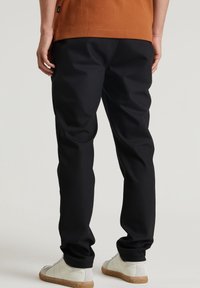 Svarta tapered-byxor gjorda av mjukt tyg, med en slät yta, elastisk midja och subtila sömdetaljer, i kombination med ljusa skor.