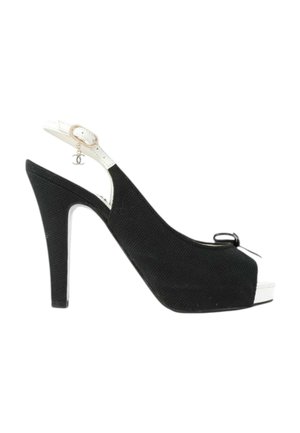 Chaussure noire à talon haut à bout ouvert, bride arrière, avec une lanière blanche et un petit pendentif logo suspendu près de la boucle de la cheville.