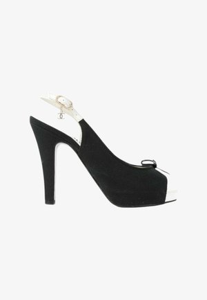 Sort stilet med åbne tæer, slingback med hvid rem og lille hængende logo-vedhæng nær ankelspændet.