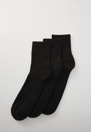 Tres pares de calcetines negros apilados verticalmente sobre un fondo blanco liso, mostrando su tejido suave y los puños acanalados.