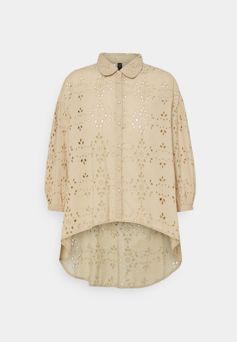 Chemise beige avec un col arrondi, présentant des découpes œillets en motifs floraux et un ourlet asymétrique ; confectionnée dans un tissu léger.