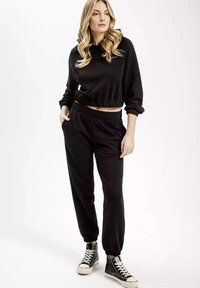 Czarna krótka bluza z kapturkiem z elastycznymi mankietami w zestawie z czarnymi dresami z elastycznym paskiem. Stylizacja uzupełniona czarnymi sneakersami za kostkę.