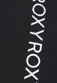 Black swim shorts with a glossy finish feature a prominent white Roxy logo vertically along the side. Elastic waistband for comfort.
