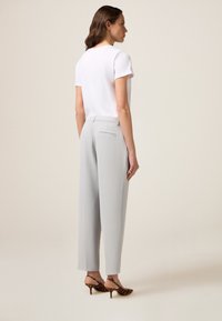 Top corto bianco a maniche corte abbinato a pantaloni a gamba larga grigi chiari a vita alta e tacchi con stampa leopardata. Tasche laterali e posteriori sui pantaloni.