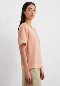 Katoenen T-shirt met korte mouwen in perzik, met een V-hals, een relaxte pasvorm en een detail aan de zoom. Draagt bij lichte onderkleding.
