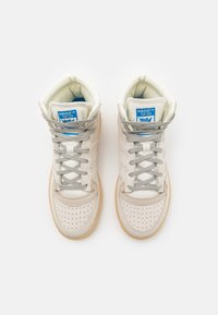 High-top sneakers in off-white leather, featuring grey laces, perforated toe box, and a gum sole, with blue 'adidas' branding on the tongue.