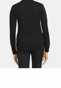 Person klädd i en svart långärmad skjorta och svarta byxor, sedd bakifrån mot en enkel vit bakgrund.