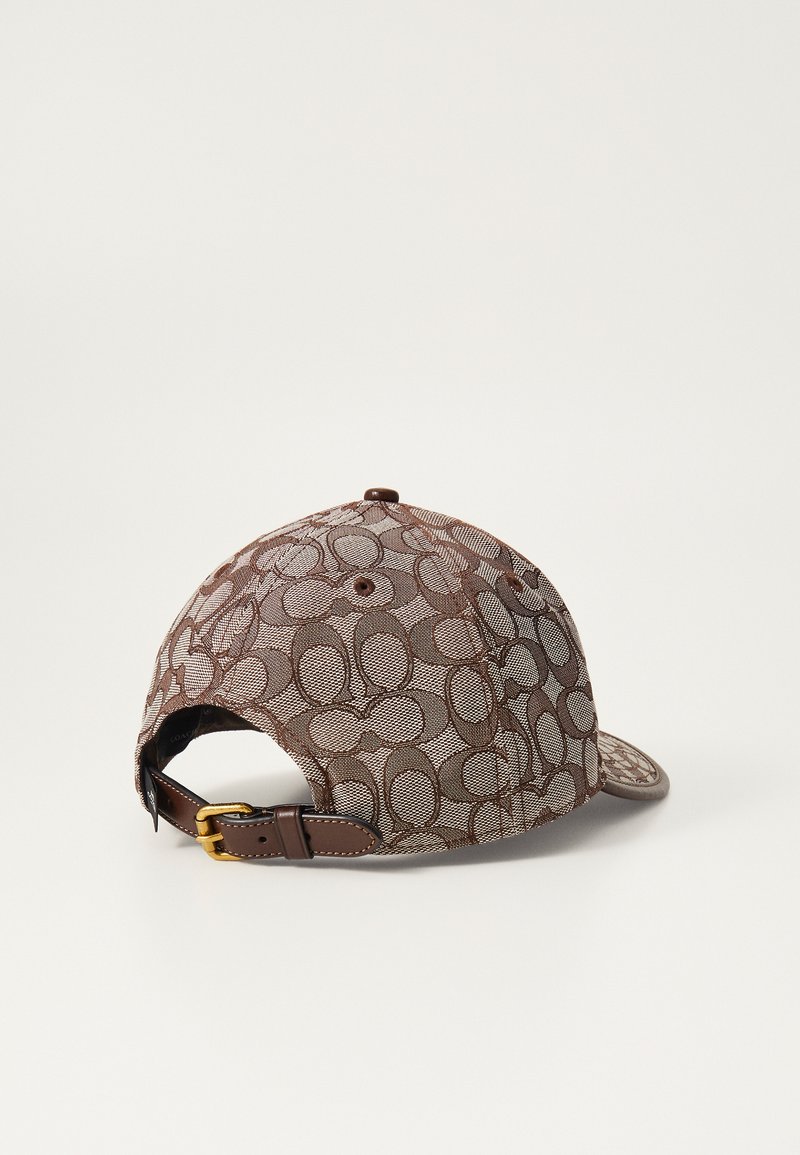 Gorra marrón con un tejido trenzado y un diseño estampado. Correa ajustable de cuero en la parte trasera con herrajes en color dorado. Superficie texturizada.