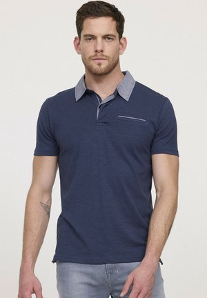 Polo-shirt bleu marine avec un col gris contrasté, des manches courtes, une poche poitrine zippée et une finition en tissu texturé.