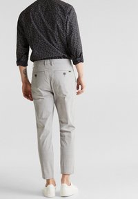 Harmaat ruutukuvioiset housut, joissa on räätälöity istuvuus, takataskut nappisulkuilla, yhdistettynä tummakuviolliseen paitaan ja valkoisiin tennareihin.