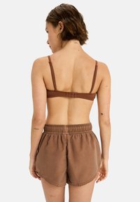 Bra in Braun mit Rippstruktur und passenden Shorts, die einen elastischen Bund und einen gewellten Saum haben. Glatte Textur mit minimaler Gestaltung.