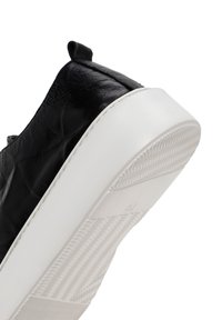 Black leather sneaker with textured upper, white rubber sole, and a reinforced heel tab. Features a traction pattern on the outsole.