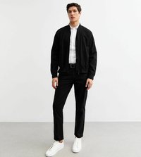 Zwarte bomberjack met een ritssluiting aan de voorkant, een staande kraag en elastische manchetten, gecombineerd met zwarte broek en witte sneakers. Glad stofoppervlak.