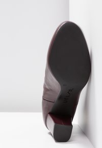 Burgundy leather high-heeled shoe with a square toe and a sturdy black rubber sole, featuring a sleek, smooth texture. Size 37.