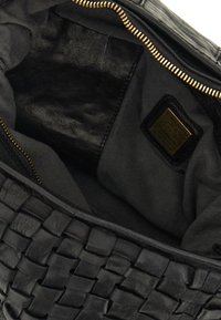 Interno di una borsa a tracolla in pelle nera intrecciata, caratterizzato da una fodera in tessuto nero liscio, cerniera dorata e una piccola etichetta con dettagli in rilievo.