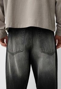 Musta farkkutakki, jossa on haalistunut tekstuuri. Ominaisuuksina on kaksi takataskua, joissa on erottuva ompelu, ja suora lahkeiden muoto.