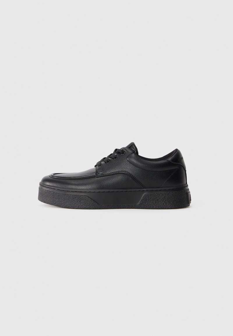 Black leather lace-up sneaker with thick textured sole, rounded toe, and low ankle height on a plain white background.