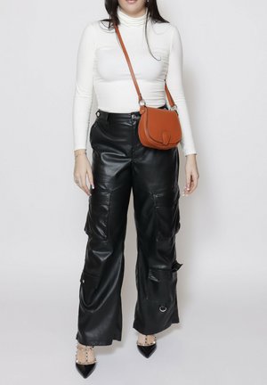 Pantaloni cargo neri in pelle con molte tasche, abbinati a un dolcevita bianco aderente e a una piccola borsa a tracolla marrone. Tacchi neri a punta.