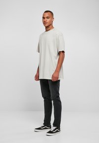 Lys grå oversized T-skjorte med korte ermer, med rund hals og subtil slitasje. Sammen med slitte mørke jeans og sorte sneakers.