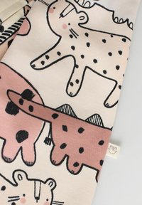 Tissu en coton présentant des motifs d'animaux amusants dans des teintes de rose doux, beige et noir. Les impressions notables incluent des taches et des rayures sur différentes formes.