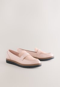 Paire de mocassins en cuir rose clair avec détail de bride perforée et semelles en caoutchouc noires sur un fond clair uni.
