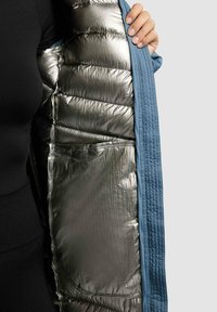 Padded jacket with a blue exterior and metallic silver lining. Features quilted texture and an interior pocket detail.