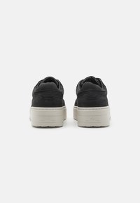 Schwarze Wildledersneaker mit dicker Cremesohle und auffälligen Nähten. Mit abgerundetem Zehenbereich und dezentem Markenlogo an der Ferse. Glatte Textur.