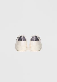 Λευκά αθλητικά παπούτσια με γυαλιστερά ασημένια διακοσμητικά στη φτέρνα, στρογγυλή μύτη, επίπεδη σόλα και σχέδιο με κορδόνια. Απαλή υφή και μίνιμαλ στυλ.