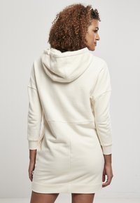 Rochie cu glugă dintr-un material moale, de culoare crem, cu mâneci lungi, buzunare laterale și un croi lejer, având manșete și tiv rigate.