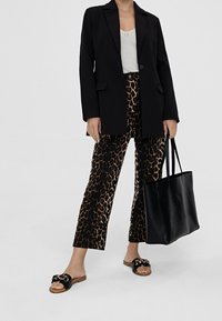 Czarna marynarka na szarym topie, do tego spodnie w panterkę, czarne sandały z ozdobnym supełkiem oraz duża czarna torba typu tote.