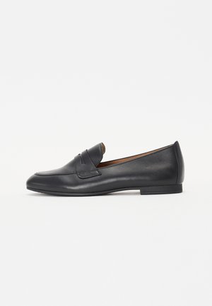 Sort læder slip-on loafer med lav hæl og remdetalje over vampen, vist fra siden på en hvid baggrund.