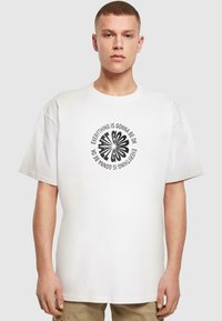 White cotton t-shirt featuring a circular black graphic print with text "EVERYTHING IS GONNA BE OK." Classic crew neckline, loose fit.